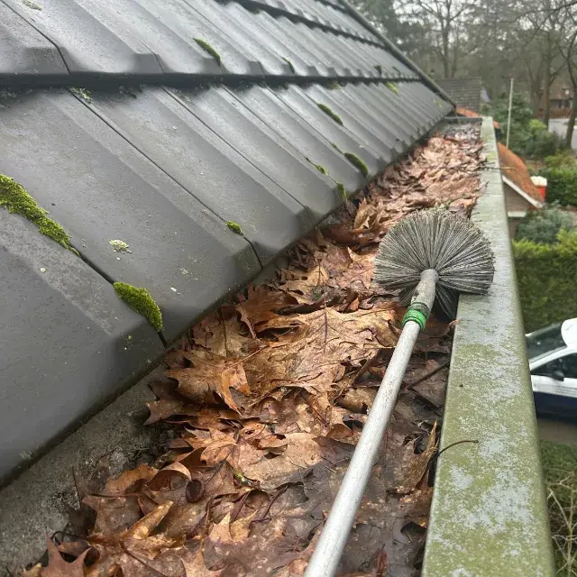 Dakgoot reinigen door bladeren en vuil handmatig te verwijderen