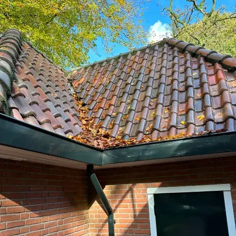 Ophoping van herfstbladeren in een kilgoot tussen twee schuine daken