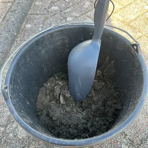 Emmer met opgehoopt vuil uit de dakgoot en een kunststof gootschep