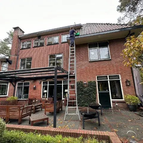 Dakgoot schoonmaken met een ladder bij een woning met een terrasoverkapping
