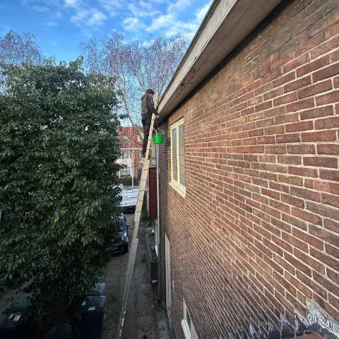 Dakgoot schoonmaken door een vakman op een ladder bij een woning