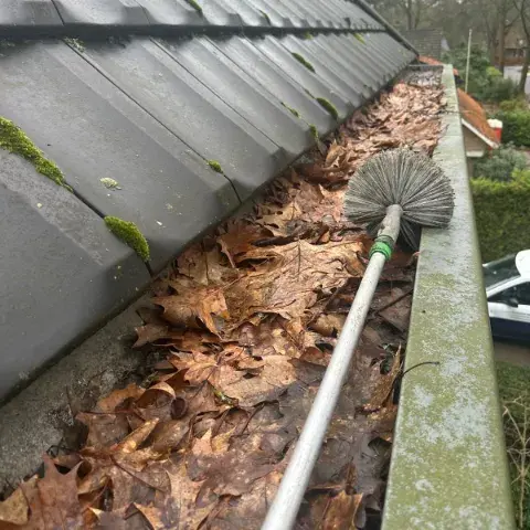 Dakgoot schoonmaken met een borstel om opgehoopte herfstbladeren te verwijderen
