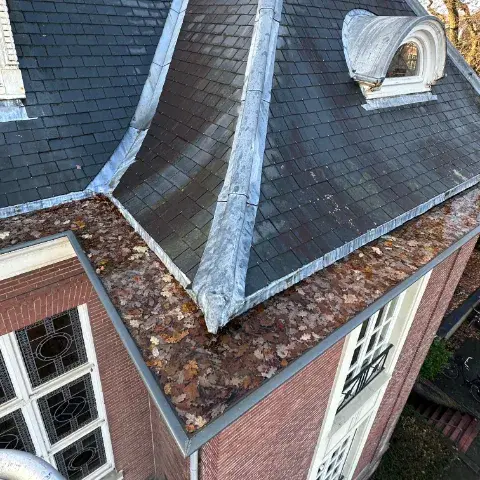 Dakgoot schoonmaken bij een mansardedak met een grote ophoping van herfstbladeren