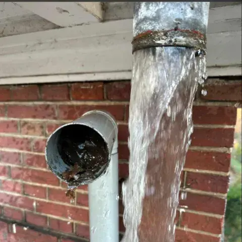 Verstopte regenpijp met bladeren waardoor regenwater langs de aansluiting stroomt