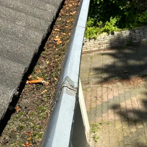 Vervuilde zinken dakgoot met opgehoopt mos, bladeren en vuil langs de dakrand